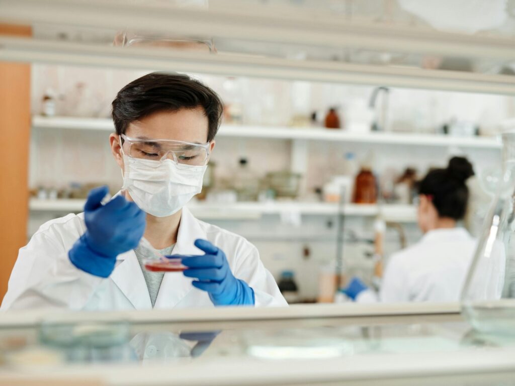 Researcher in a lab coat working on a scientific experiment with a petri dish and protective gear.