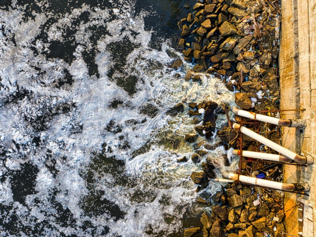 Aerial view of polluted water flowing through pipes into a Jakarta river, causing environmental concerns.