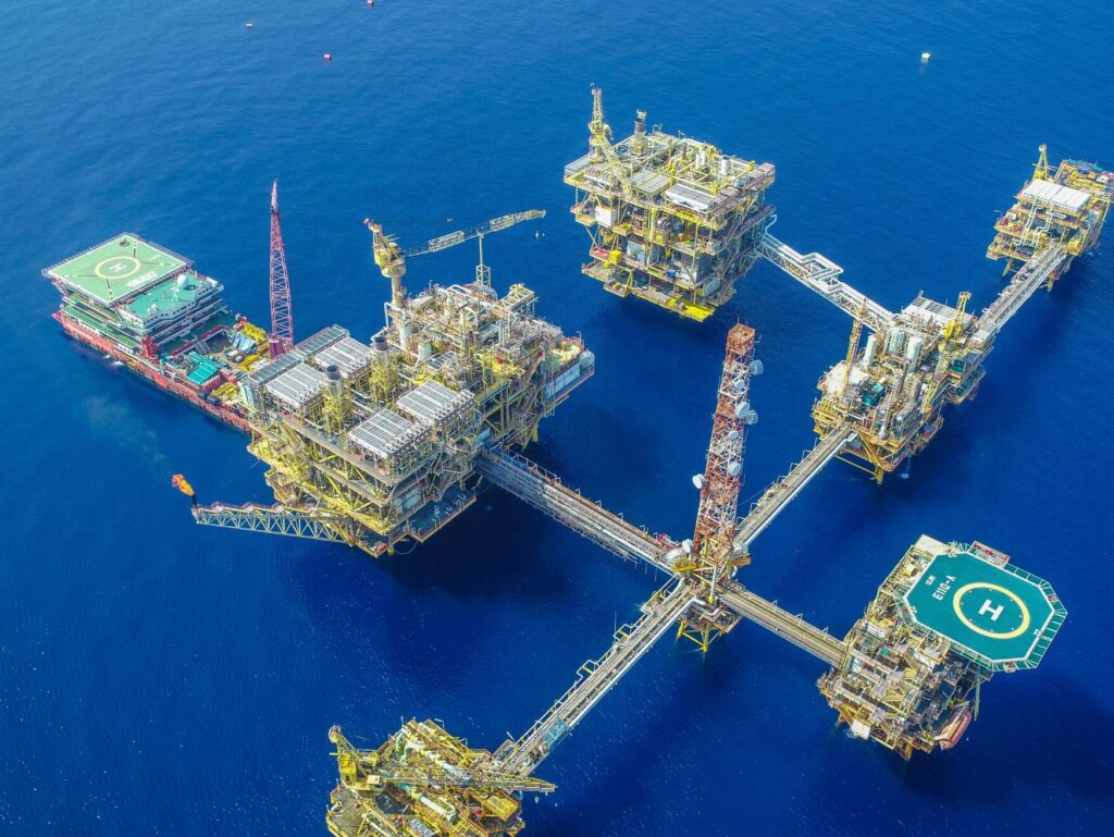 Drone shot of a large, complex offshore oil platform in deep blue ocean waters.